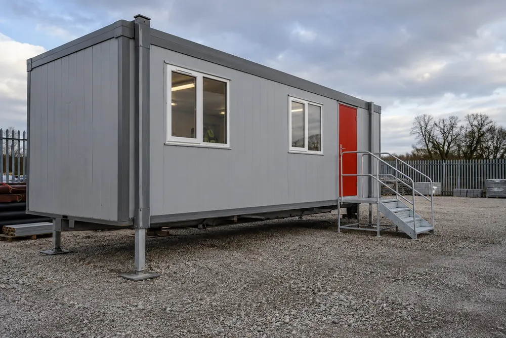 Grey steel site cabin with red door and metal access steps